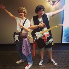 two people standing next to each other in front of a projector screen holding guitars