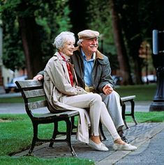 an older couple sitting on a bench in the park smiling at each other's eyes