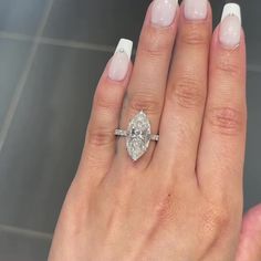 a woman's hand with a diamond ring on top of her finger and white nails