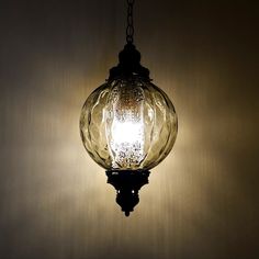 a glass light hanging from a chain on a wall in a room with dark lighting