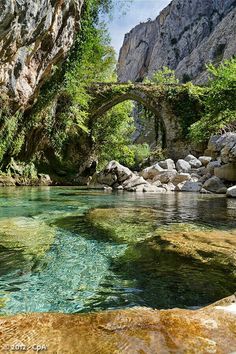 the water is crystal clear and blue in this mountain stream, with an old stone bridge over it