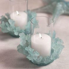 two clear glass vases filled with white candles on top of a cloth covered table