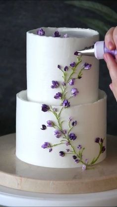 someone is decorating a three tiered cake with purple flowers