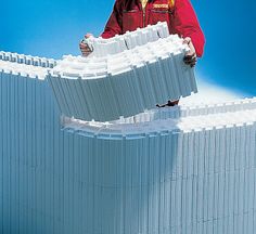 a man in red jacket standing next to large white building model on blue background,