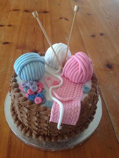 a cake decorated with yarn, buttons and knitting needles on top of a wooden table