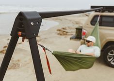 a man sitting in a hammock on the beach next to a truck with his feet propped up