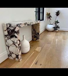 a white vase sitting on top of a wooden floor next to a black and white table