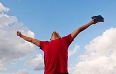 a man in red shirt flying a kite with his arms wide open and hands raised