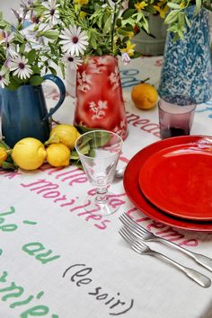 the table is set with red plates, silverware and vases filled with flowers