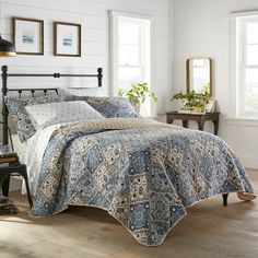 a bed with a blue and white comforter in a room next to two windows