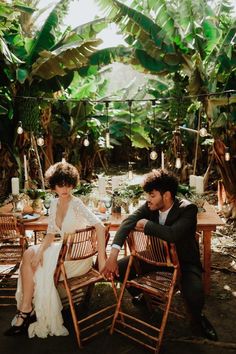 a man and woman sitting at a table in the middle of a jungle with palm trees