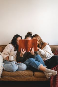 three people sitting on a couch with a book in front of them and one person holding a coffee mug