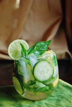 a cucumber and mint drink in a glass on a green cloth with a brown background