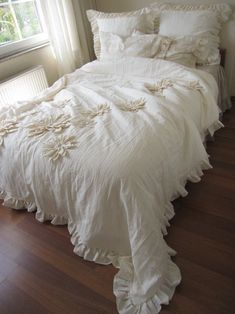 an unmade bed with white sheets and ruffles on the comforter is in front of a window