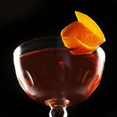 an orange peel sitting on top of a drink in a glass filled with liquid and garnish