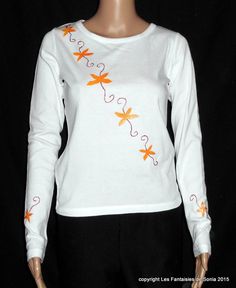 Long-sleeved white cotton t-shirt size 36 for women or teenagers. Length: 56 cm. Chest measurement: 76 cm. Sleeve length: 65 cm. Design hand-painted directly on the garment with glittery orange and pink fabric paint. Stylized floral pattern on the front diagonally and a stylized flower on the bottom of each sleeve. The t-shirt was not made by me. Machine washable at 30o and iron the pattern on the reverse side. Fitted Cotton Long Sleeve Top, Fitted White T-shirt For Fall, White Fitted T-shirt For Fall, White Long Sleeve T-shirt For Fall, White Fitted Cotton Long Sleeve Top, Fitted White Cotton Long Sleeve Top, White Cotton Crew Neck Long Sleeve Top, White Cotton Long Sleeve Crew Neck Top, White Long Sleeve Cotton T-shirt