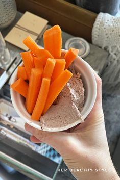 a person holding up a bowl with carrots on it