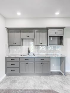 an empty kitchen with gray cabinets and marble counter tops in the middle of the room