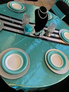 the table is set with blue and white plates, silver place settings, and a necklace on it