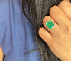 Introducing our Phalgun Emerald Adjustable Statement Ring, a stunning piece of jewelry that showcases the beauty of lab-grown emeralds. This ring features a large, vivid green emerald, capturing the essence of the lush green forests and bringing a pop of color to any outfit. The emerald is a lab-grown stone, ensuring that it is ethically sourced and environmentally friendly. This ring is the perfect cocktail ring, making a statement at any special occasion. The adjustable design allows for a comfortable fit, ensuring that the ring stays in place no matter what the night brings. The emerald is associated with the Anahata chakra, known for its ability to bring balance and harmony to the mind and body. Wearing this ring is not only a fashion statement, but also a way to tap into the spiritual Green Emerald Ring With Accent Stones For May Birthstone, Green Emerald Cut Ring With Halo Setting, Fine Jewelry Green Emerald Ring With Accent Stones, Green Emerald Rings With Accent Stones, Green Emerald Cut Ring With Accent Stones, Green Emerald Rings With Halo Setting, Gia Certified Green Emerald Ring In Fine Jewelry Style, Gia Certified Green Emerald Ring For Promise, Gia Certified Green Emerald Promise Ring