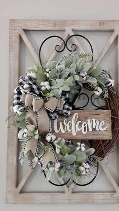 a wreath with the word welcome is hanging on a wooden frame in front of a wall