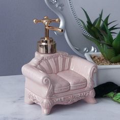 a pink chair soap dispenser sitting on top of a counter next to a potted plant