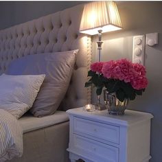 a white bed topped with pink flowers next to a night stand