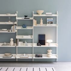 a white shelf with books and vases on it next to a wall mounted lamp