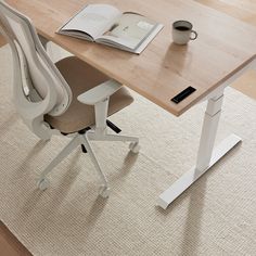 an office desk with a book, coffee cup and pen on it next to a chair