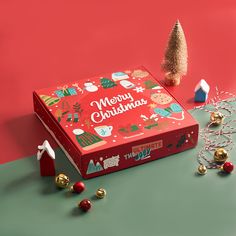 an open christmas box with ornaments and decorations around it on a green surface next to a small tree