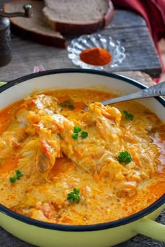 a bowl filled with chicken and cheese soup on top of a wooden table next to bread