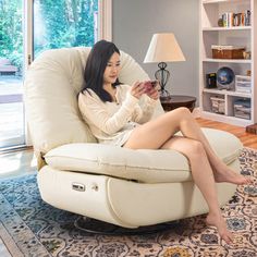 a woman sitting in a chair with her legs crossed, reading a book and looking at her phone