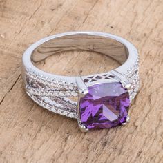 an amethyst purple stone surrounded by white diamonds on a wooden surface in a ring