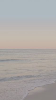 a person walking on the beach with a surfboard in their hand and an ocean behind them