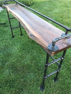 a wooden bench sitting on top of a green grass covered field next to a metal pipe