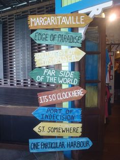 there are many signs on the pole in front of a building that says margaritaville edge of paradise, far side of the world, port of the clock, port of indecion, port of immersion, st