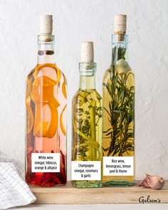 three bottles filled with different types of liquid and herbs next to each other on a table