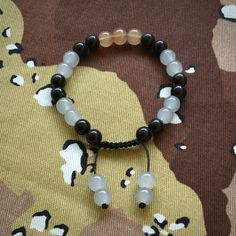 a black and white beaded bracelet with two beads on it sitting on a camouflage background