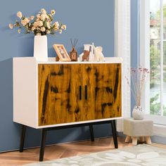 a white and brown cabinet with flowers in vases on it next to a blue wall