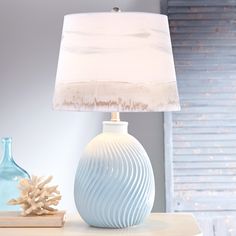 a white lamp sitting on top of a table next to a blue vase and a sea urn