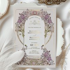 an ornate wedding card is displayed on a table with white and gold decorations, feathers, and other items