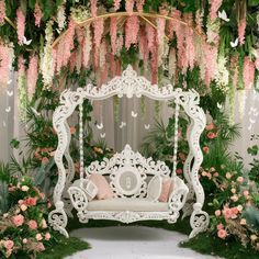 an ornate white bench with pink flowers and greenery around it, surrounded by lush green foliage