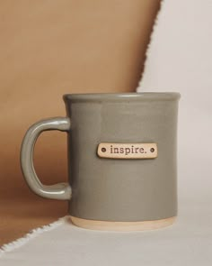 a gray coffee mug with a wooden name tag sitting on top of a white table cloth