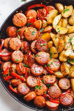 a skillet filled with potatoes and sausages on a marble counter top, topped with parsley