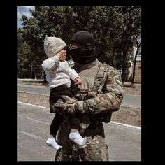 a soldier holding a baby in his arms while standing next to a man with a mask on