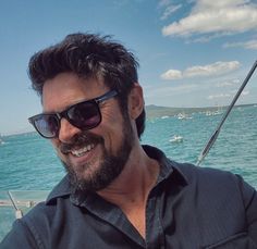 a man wearing sunglasses is sitting on a boat in the water and smiling at the camera