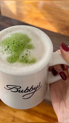 a woman holding a cup with green liquid in it and the words bubbly written on it