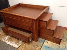 a wooden box sitting on top of a floor next to some drawers and steps in front of a wall