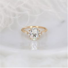 an engagement ring with three stones on it, sitting on a white surface in front of some feathers