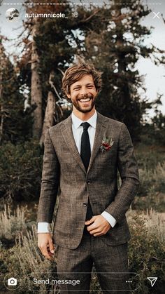 a man wearing a suit and tie standing in front of some trees with his hands in his pockets